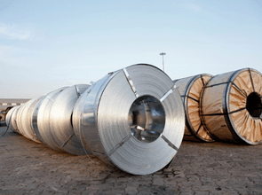 Row of large metal steel coils lying on a cracked paved yard at an outdoor industrial site