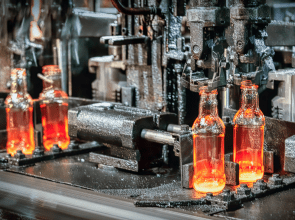 Industrial bottling line filling and capping glass bottles with orange liquid on a conveyor.