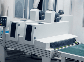 Industrial white automated machine with two vertical control panels on a conveyor belt in a bright factory setting.